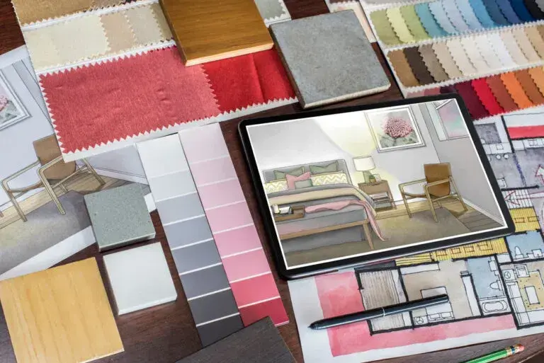 Overhead view of an interior designer's desk with swatches, palettes, samples, and a tablet showing a room design.